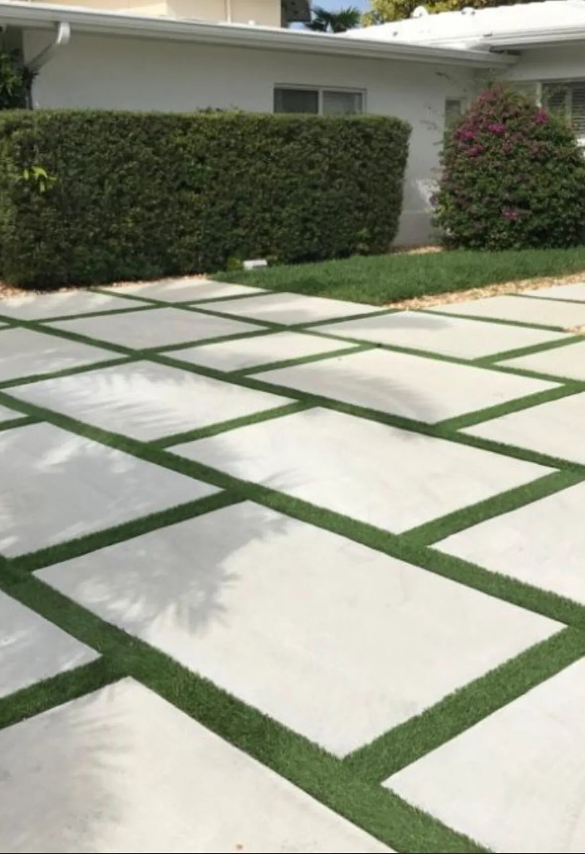 Large concrete pads with artificial turf strips in a front yard